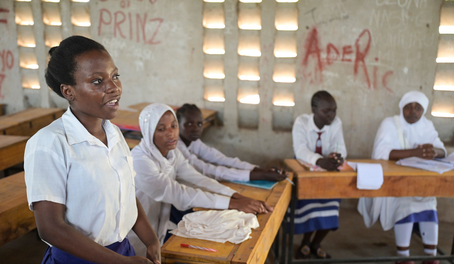 Schülerinnen an der Blue State Secondary des JRS in Kenia sitzen in einem Klassenzimmer. Ein Mädchen im Vordergrund steht und spricht in Richtung Tafel nach vorne.