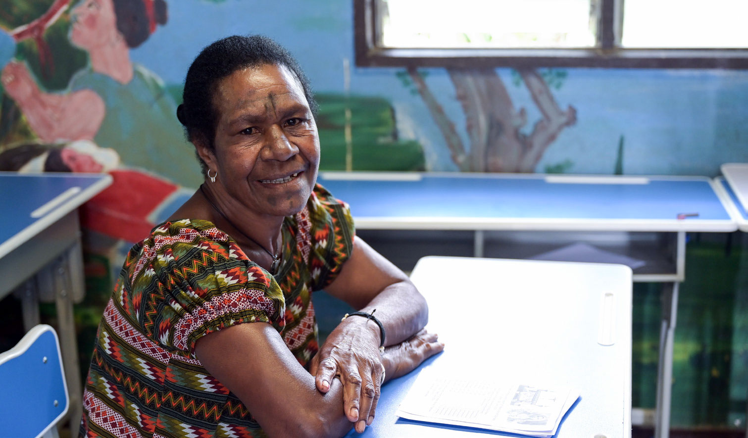 Eine erwachsene Frau sitzt in einer Schulbank in Papua-Neuguinea und lächelt in die Kamera.