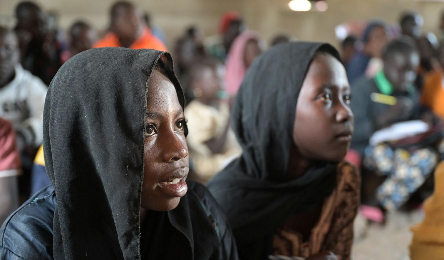 Zwei Mädchen mit schwarzen Kopftüchern blicken in einem improvisierten Unterrichtsraum in einem Flüchtlingscamp im Südsudan zur Tafel