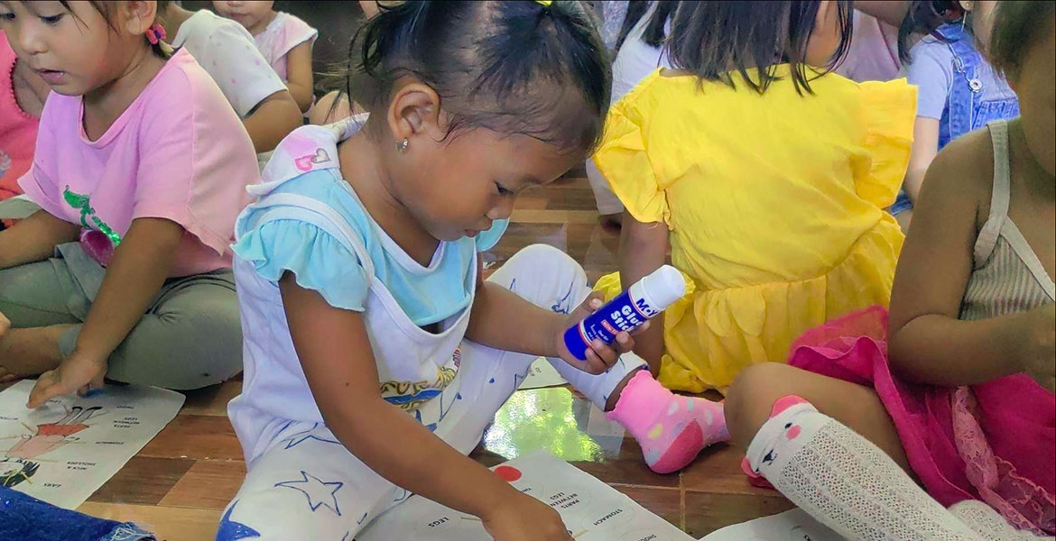 Kinder spielen auf dem Fußboden sitzend in der Kinderhilfseinrichtung von ANCE auf den Philippinen.