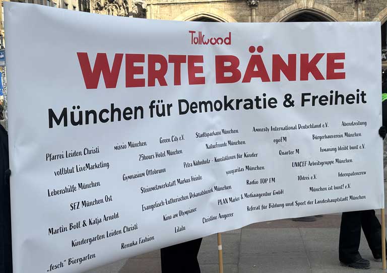 Großes Plakat mit der Aufschrift Tollwood Werte Bänke München für Demokratie und Freiheit sowie den Namen der Partnerinnen und Partner der Wertebänke