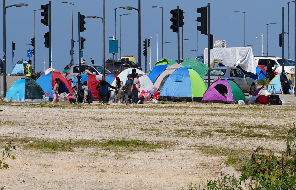 Bunte Zelte stehen auf einem sandigen, kärglich bewachsenen Platz. Im Hintergrund zahlreiche Ampeln und der strahlend blaue Himmel.