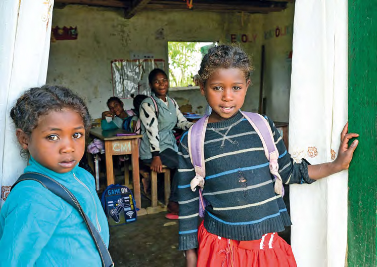 Zwei kleine Mädchen im Grundschulalter stehen im Türrahmen zu einem Klassenraum und blicken in die Kamera