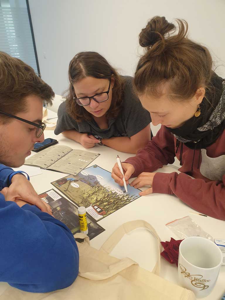 Drei Schüler sind über eine Schulbank gebeugt und bearbeiten konzentriert ein Arbeitsblatt.