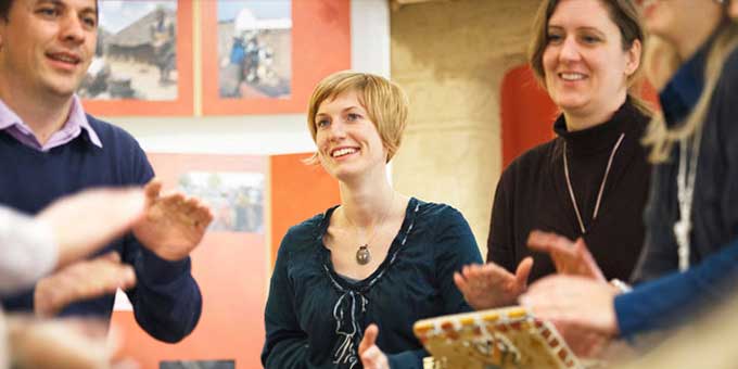 Ein Mann und zwei Frauen sitzen im Ausstellungsraum von missio-München und trommeln.