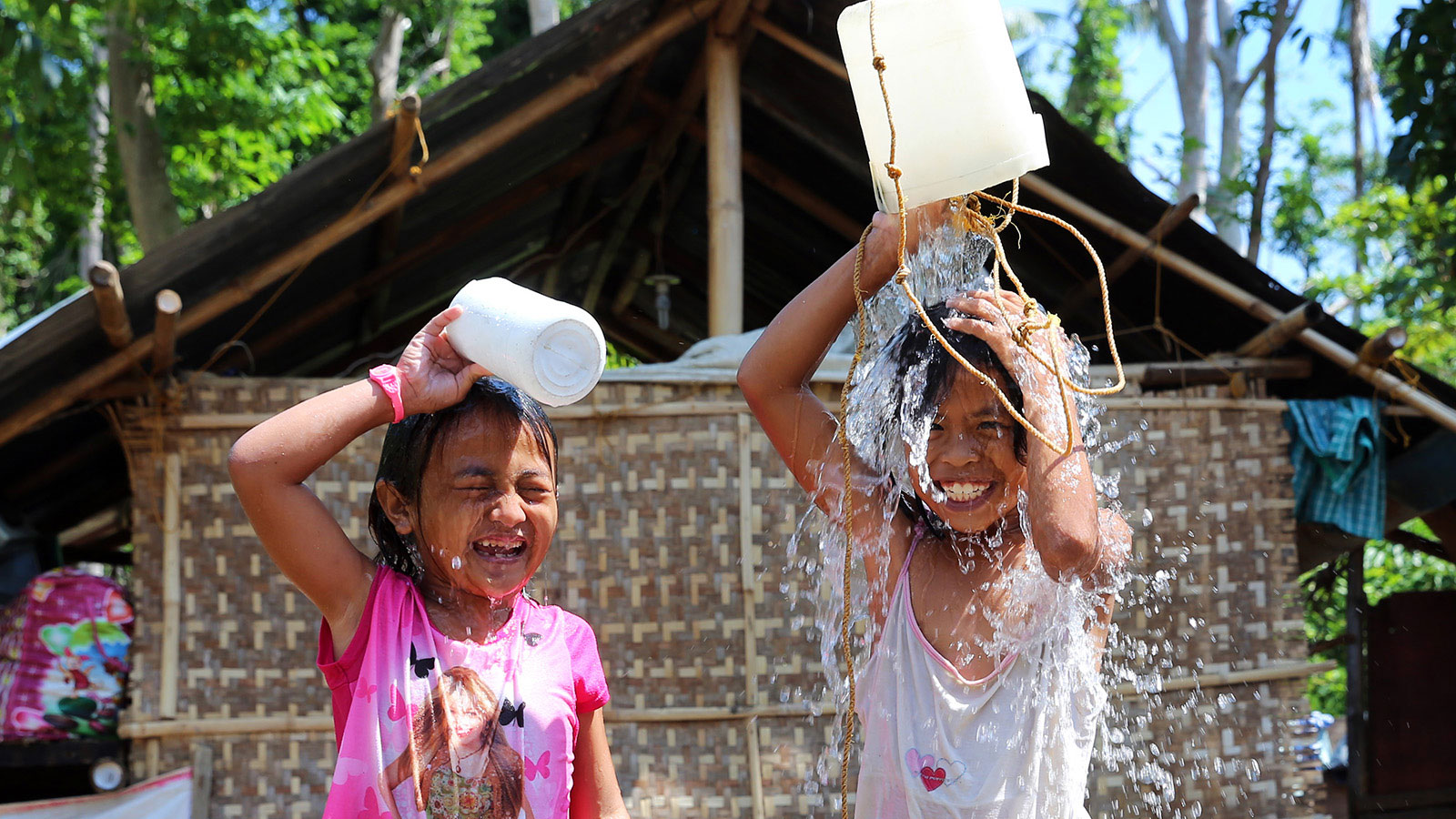 Zwei Mädchen schütten lachend Wasser über ihre Köpfe