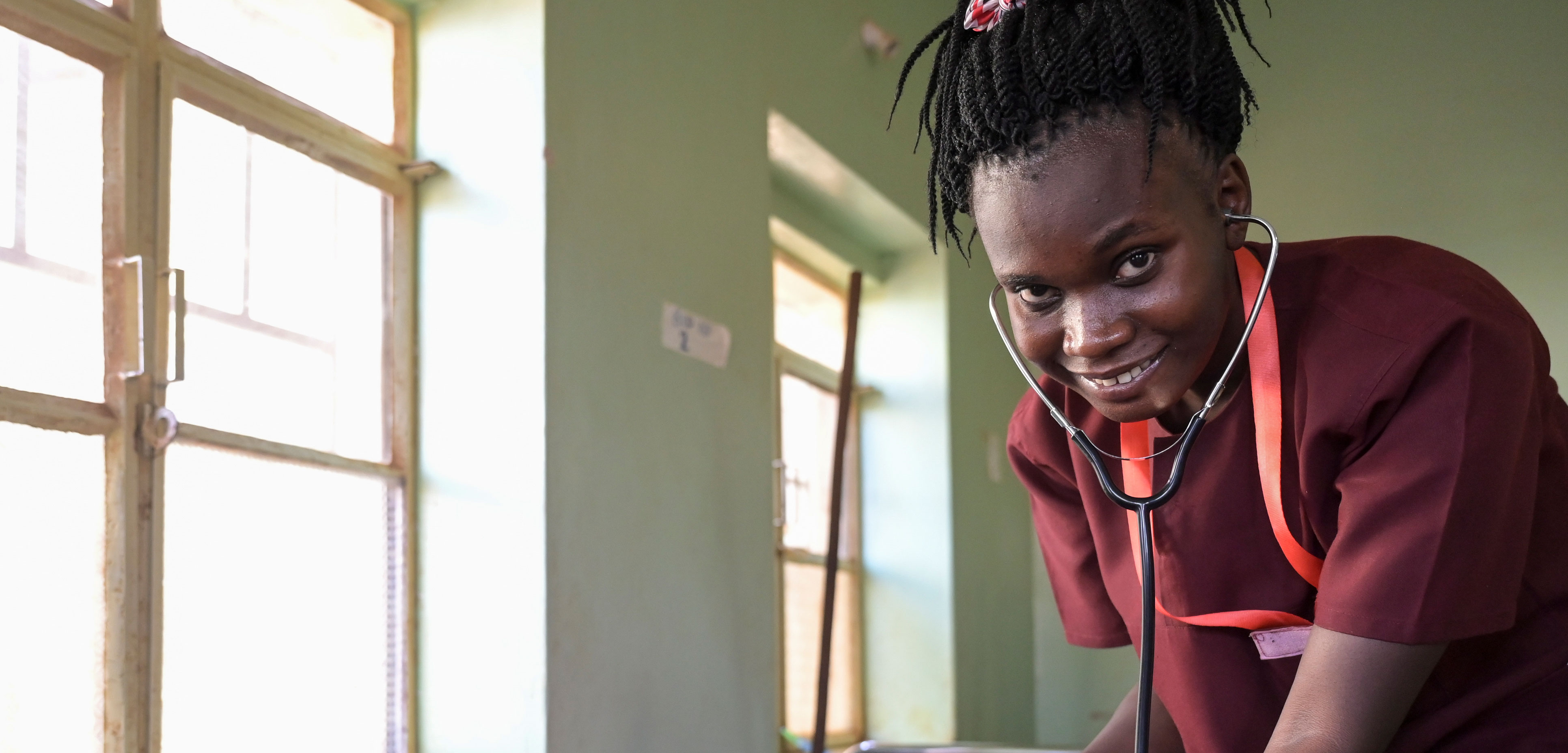 Die Südsudanesin Edia Atanasio Mustafa blickt lachend in die Kamera, während sie im Zuge ihrer Ausbildung zur Hebamme Herztöne abhört