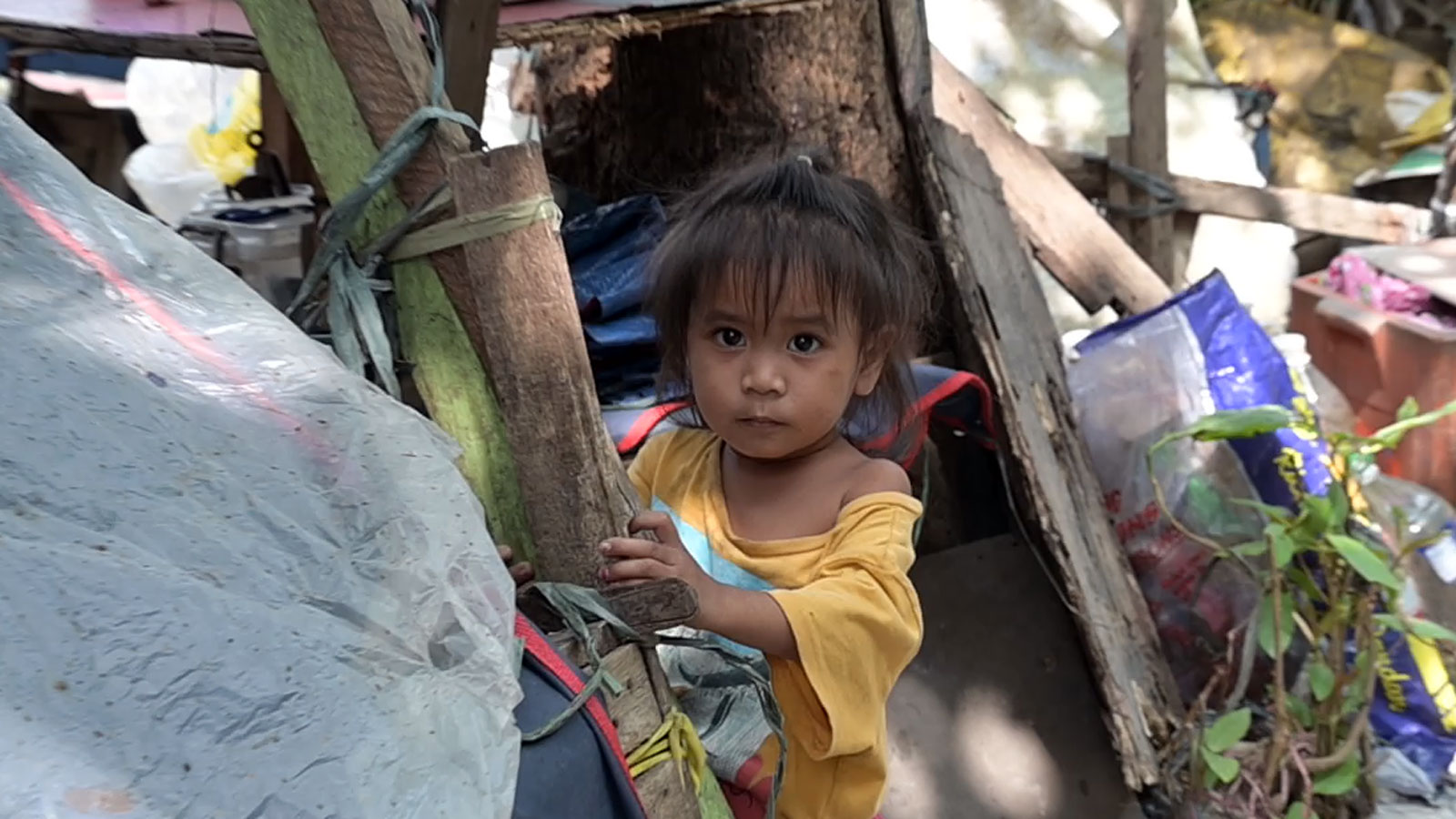 Ein Straßenkind blickt ängstlich aus einem Verschlag in vermüllter Umgebung auf den Philippinen.
