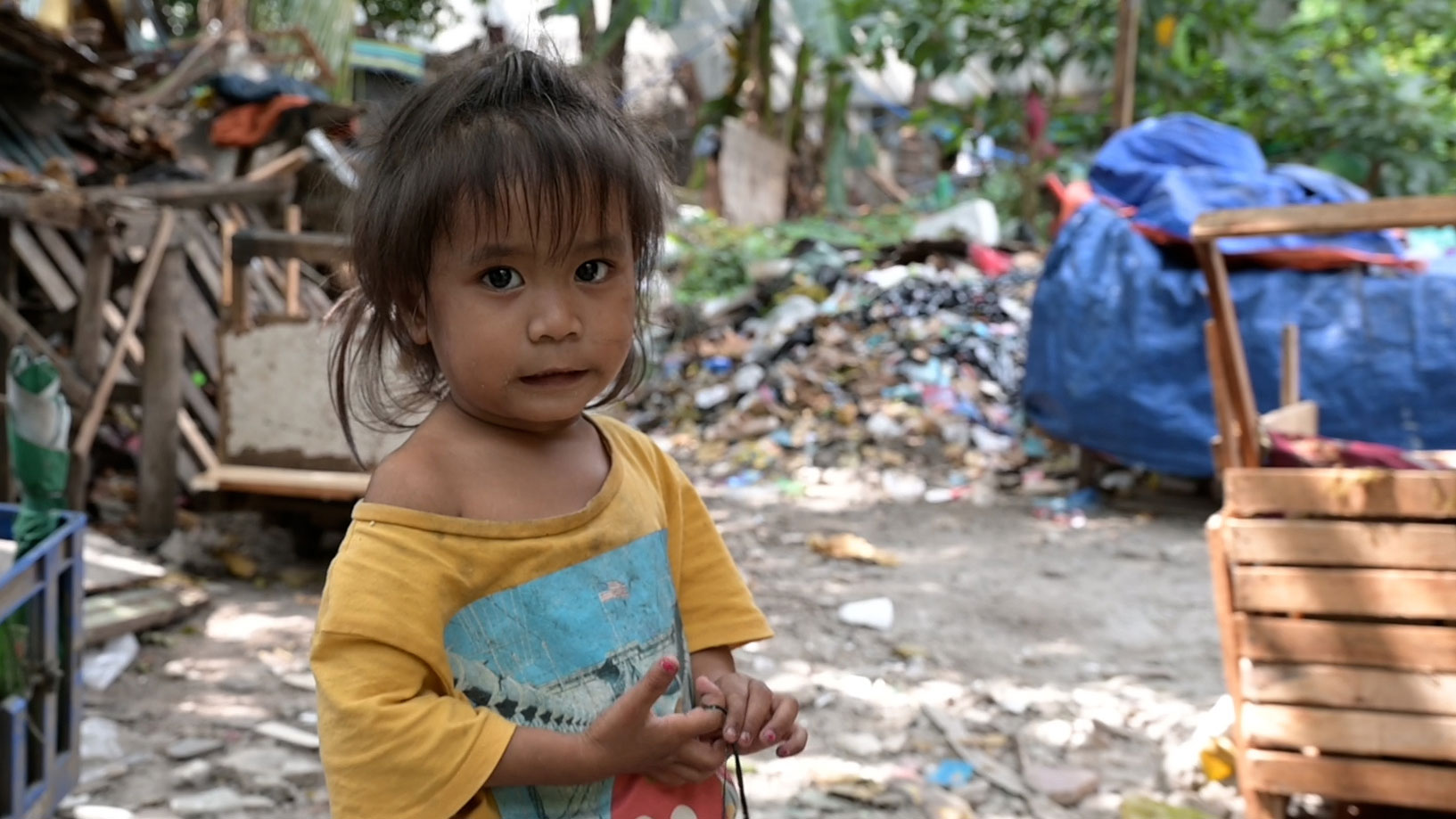 Josi, ein kleines Mädchen von den Philippinen in schmutziger Kleidung, steht in einer Gegend mit viel Müll