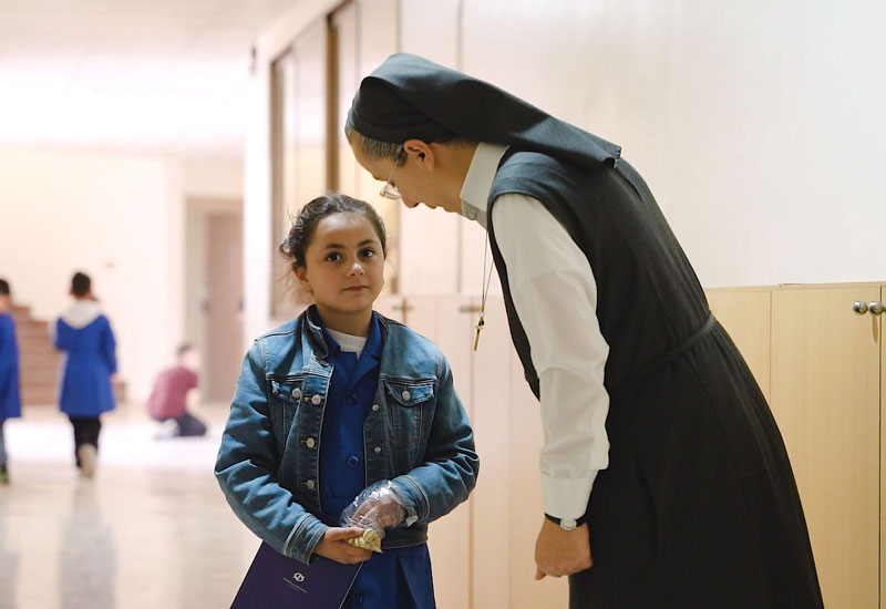 Schwester Johan spricht mit einem kleinen Mädchen im Schulgang
