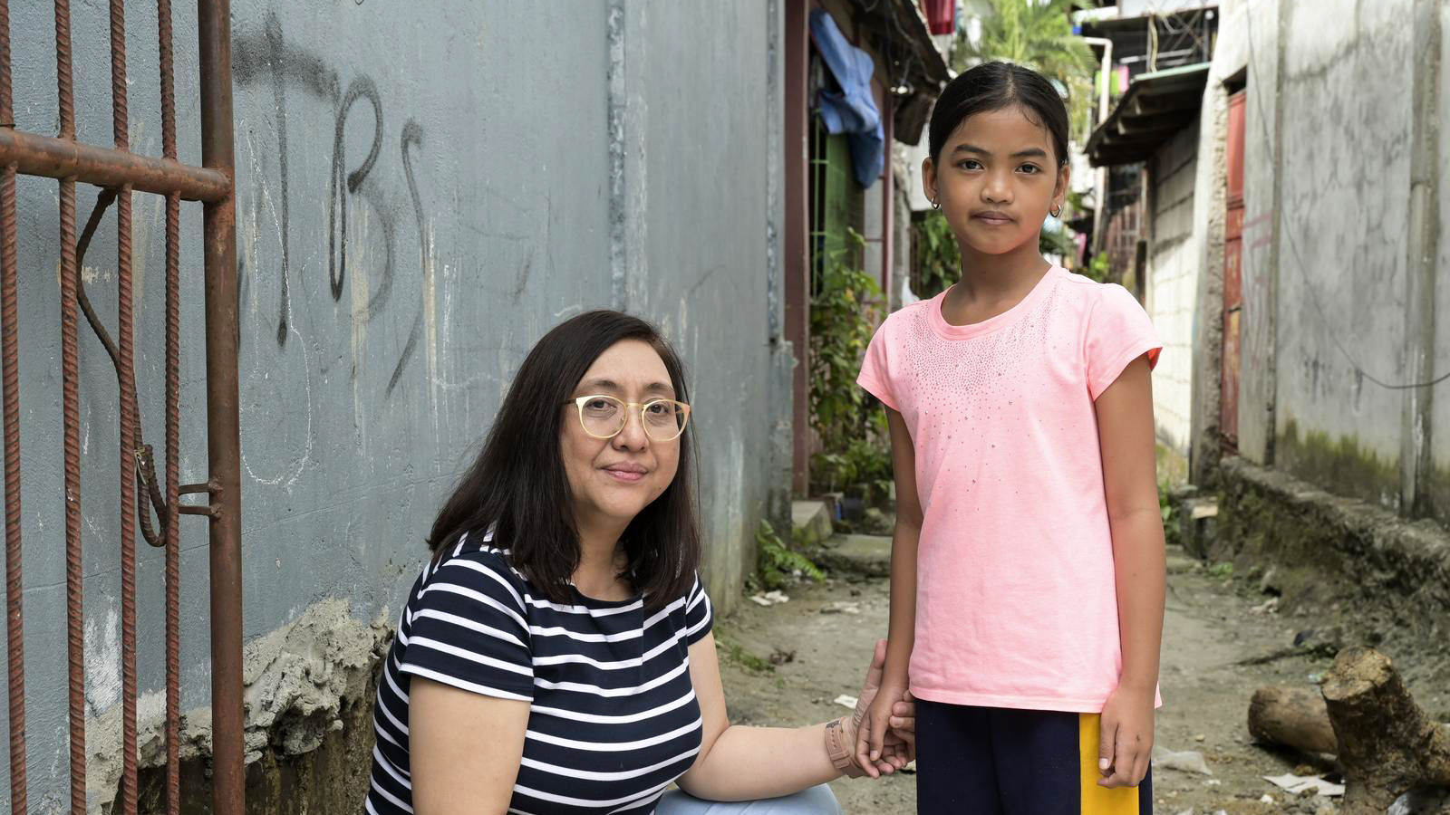 missio-Projektpartnerin Carol Daria, in der Hocke, hält die Hand von Yessa. Sie sind in einer Gasse in Payatas