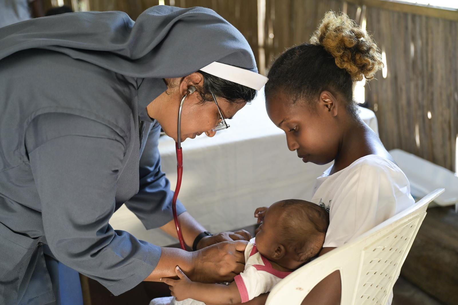 Sr. Jain Mary untersucht das Baby auf dem Schoß seiner Mutter