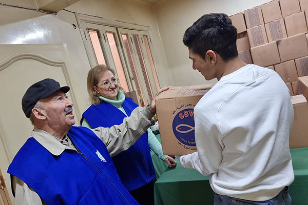 Zwei Helfer in blauen Westen geben einem Mann ein Paket mit Essen