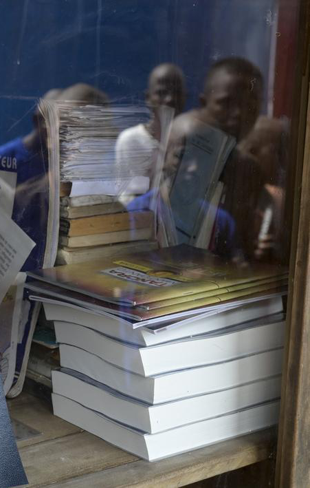 Ein Bücherschrank mit Büchern hinter einer Glasscheibe in einem Gefängnis auf Madagaskar. In der Scheibe spiegeln sich die Gesichter von Gefängnisinsassen.