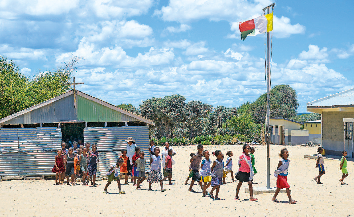Kinder strömen aus einer kirchlichen Schule, vor der die Flagge von Madagaskar weht.