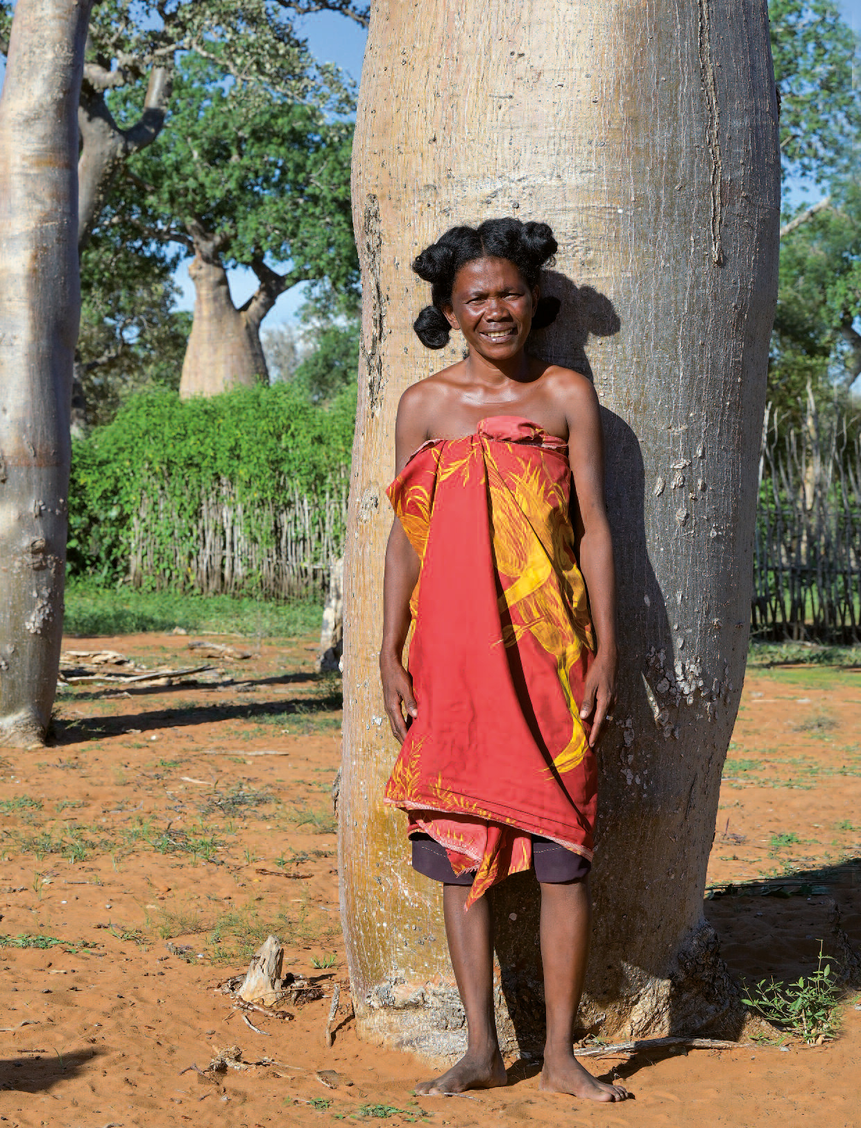 Der Titel des missio magazin 05/2026 zeigt eine Frau, die mit nackten Füßen und einem rot-gelben Tuch bekleidet vor einem alten Baobab steht.