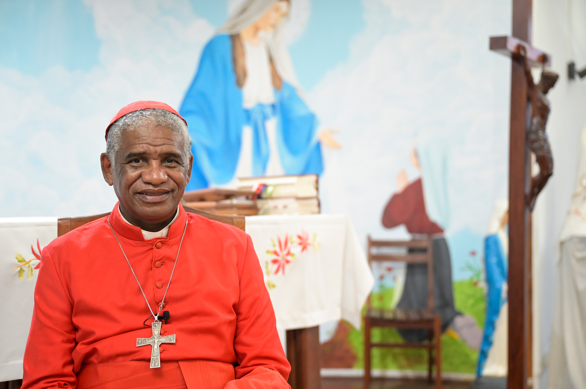 Kardinal Désiré Tsarahazana in roter Soutane und mit Bischofskreuz um den Hals sitzt in einem Kirchenraum.