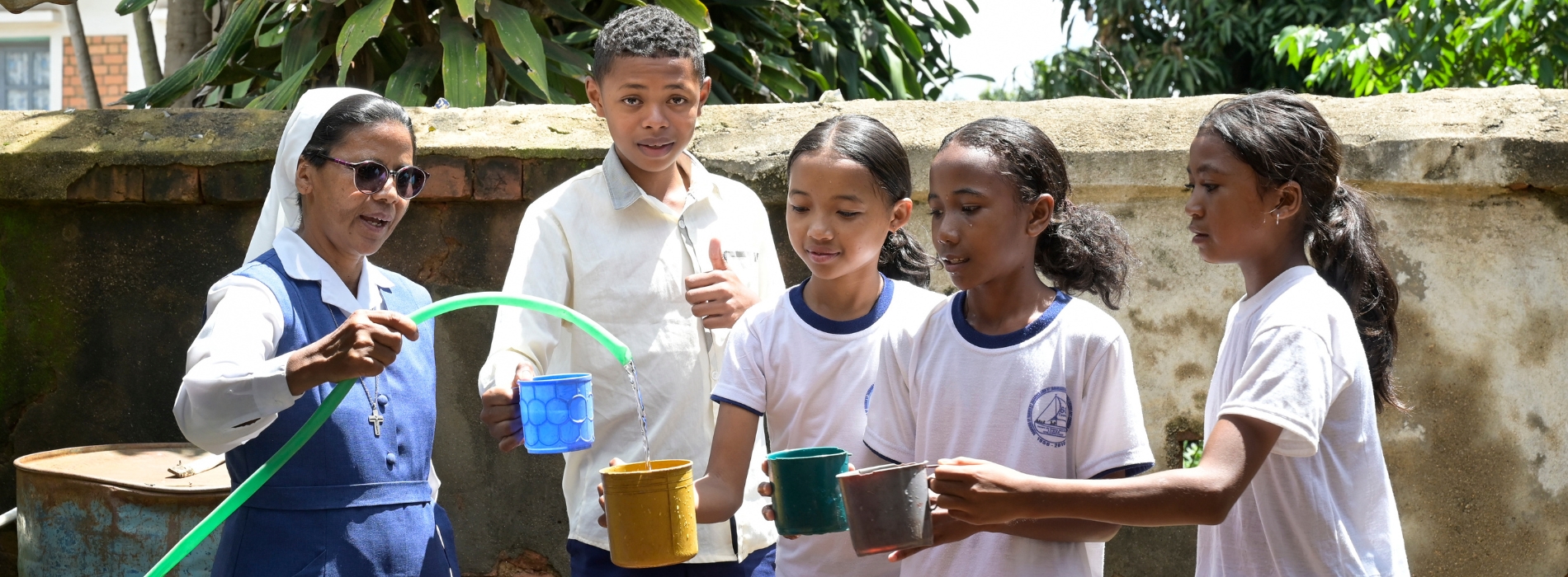 missio-Projektpartnerin Schwester Rolandine (ganz links im Bild) gießt mit einem Schlauch Wasser in die Becher von vier Schülerinnen ihrer Schule.