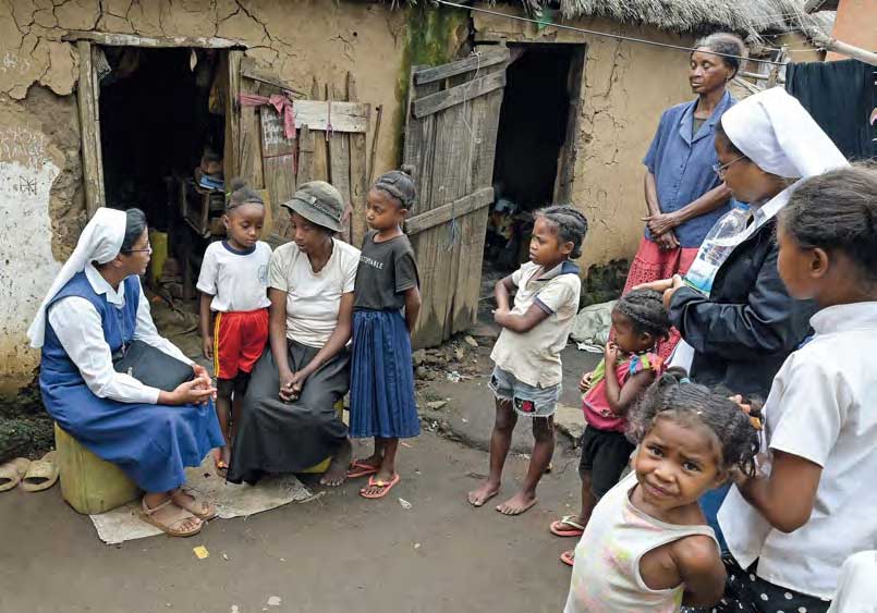 Schwester Rolandine und ihre Mitschwestern besuchen eine Familie im Umland. Schwester Rolandine im Gespräch mit einer Frau und ihren beiden Kindern vor einer Lehmhütte.