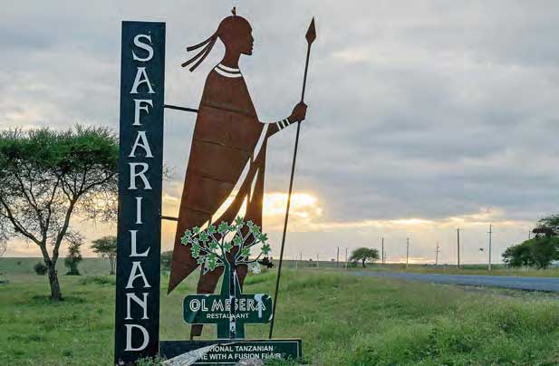 Ein großes Schild im Ngorongoro-Gebiet in Tansania mit der Aufschrift "Safariland". Daneben ist die überlebensgroße Silhouette eines Massaikriegers.