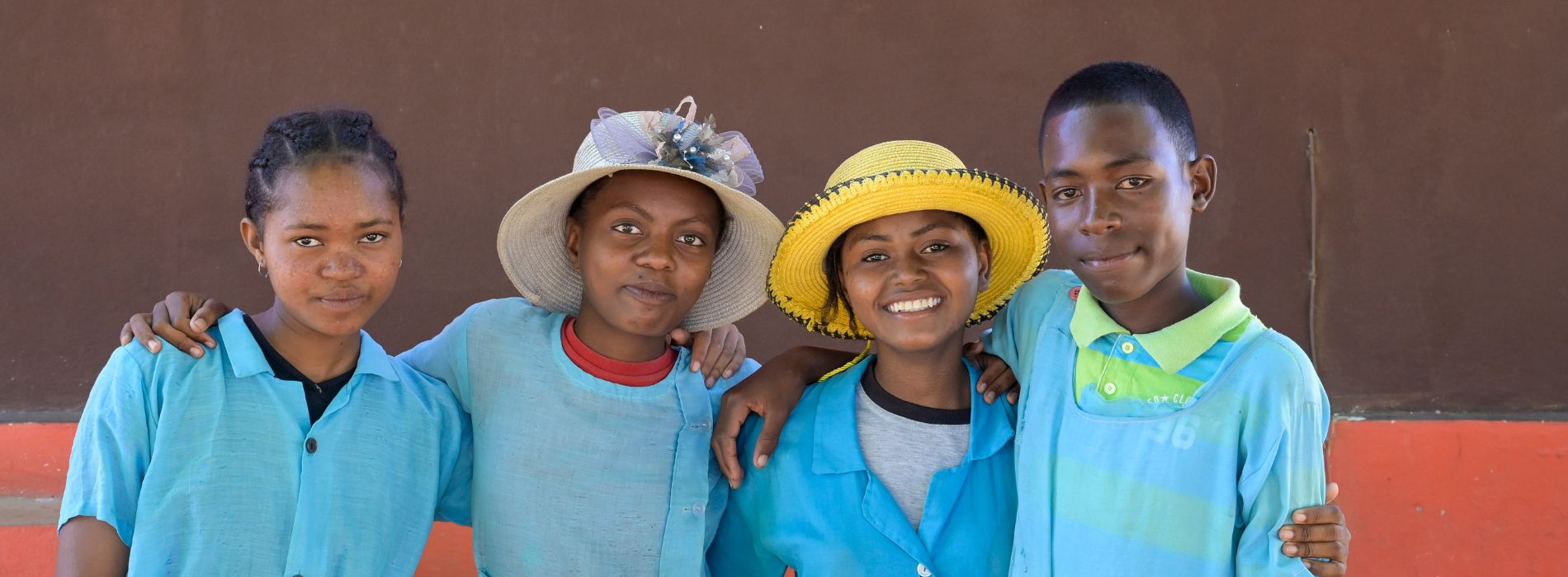Gruppenporträt von drei Mädchen und einem Jungen aus Madagaskar mit hellblauer Schulkleidung. Die beiden Jugendlichen in der Mitte tragen einen Strohhut.
