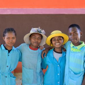 Gruppenporträt von drei Mädchen und einem Jungen aus Madagaskar mit hellblauer Schulkleidung. Die beiden Jugendlichen in der Mitte tragen einen Strohhut.