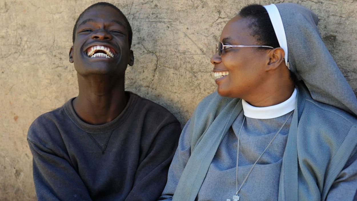 Schwester Pascalena aus Sambia und der Aids-Waise David sitzen nebeneinander und lachen.