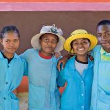 Gruppenporträt von drei Mädchen und einem Jungen aus Madagaskar mit hellblauer Schulkleidung. Die beiden Jugendlichen in der Mitte tragen einen Strohhut.
