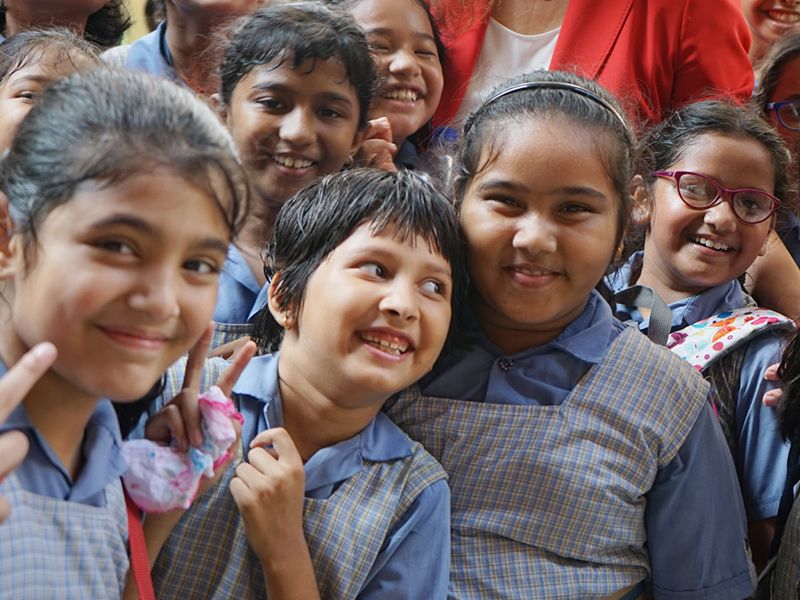 Indische Schülerinnen lächeln in die Kamera. Zwei von ihnen zeigen das Victory-Zeichen.