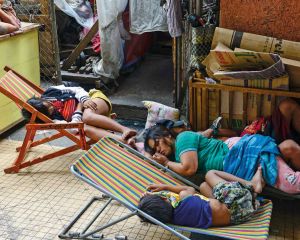 Eine Frau schläft mit ihren Kindern am Rand einer Straße in Manila auf einem Bretterverschlag. Zwei Kinder schlafen auf Klappstühlen.