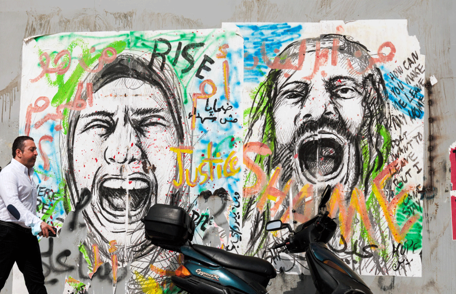 Ein Mann geht auf einer Straße in Beirut an bemalten Wänden vorbei. Die Graffiti zeigen schreiende Menschen - Symbolbild für die Notlage im Libanon