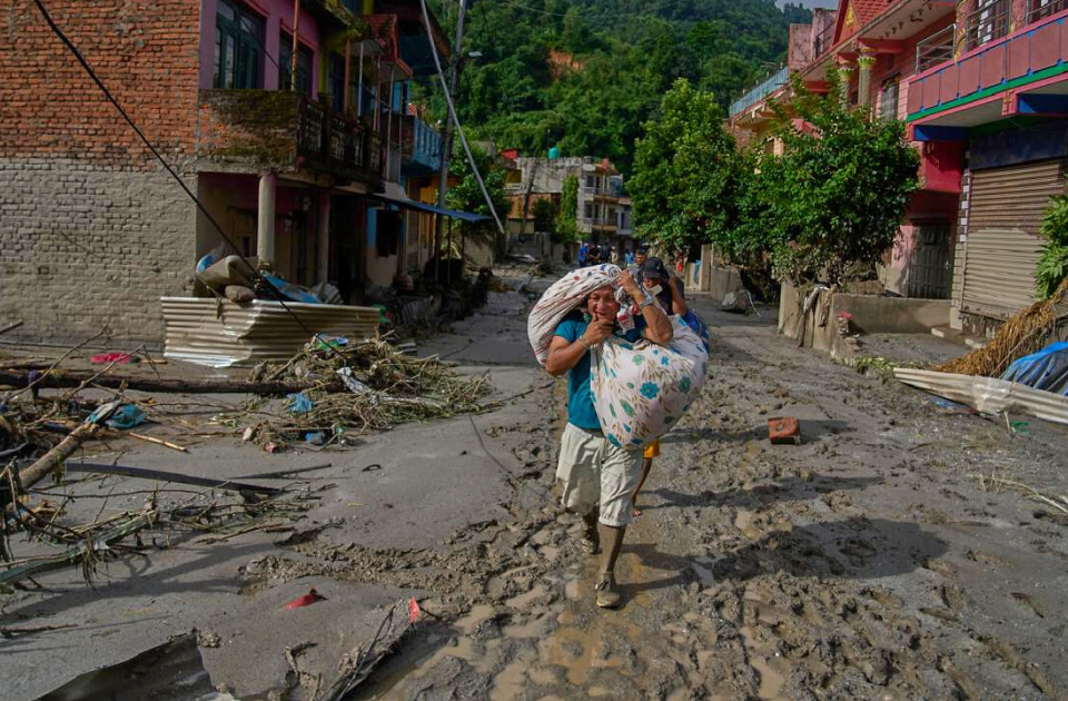 Ein Mann läuft auf von der Sturzflut in Nepal zerstörten Straße eines Dorfes der Kamera entgegen. Er trägt in Bündeln seine Habseligkeiten über den Schultern.