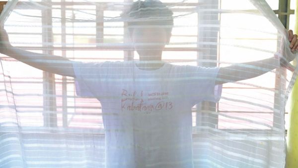 Ein Kind, das im Schutzhaus untergekommen ist, steht hinter einem halbtransparenten Vorhang, den es mit beiden Händen hält.