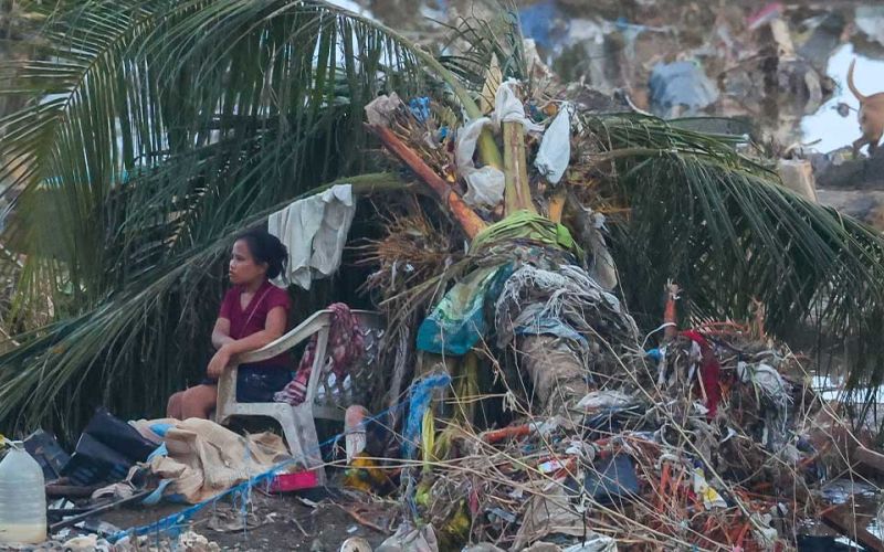 Nach dem verheerenden Taifun Kalmaegi auf der philippinischen Insel Cebu sitzt eine Frau in einem Plastikstuhl unter den Blättern einer umgestürzten Palme. Um sie herum Trümmer, Geröll, Kleiderfetzen und Chaos.