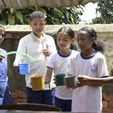 Schwester Rolandine steht mit vier Schülerinnen hinter einem Brunnen in einer Schule in Analavory in Madagaskar und gießt mit einem Schlauch frisches Wasser in die Becher der Kinder.