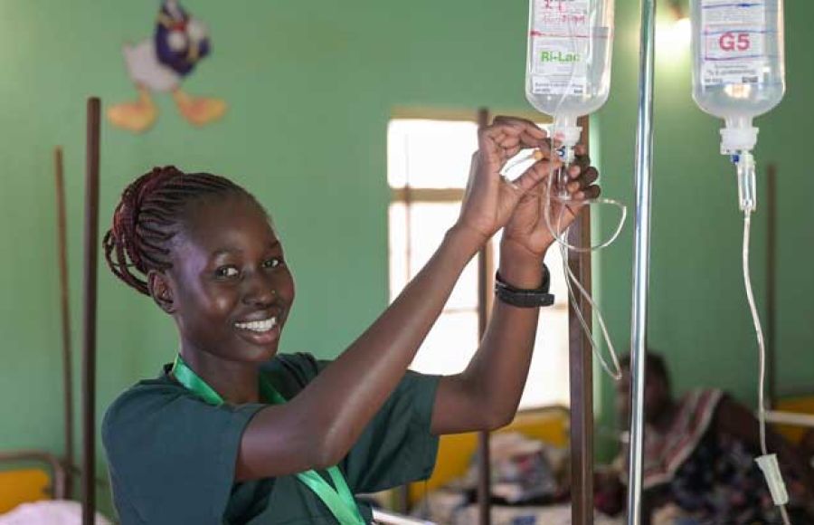 Eine junge Krankenschwester aus dem Südsudan schließt eine Infusionskanüle an und lacht in die Kamera.