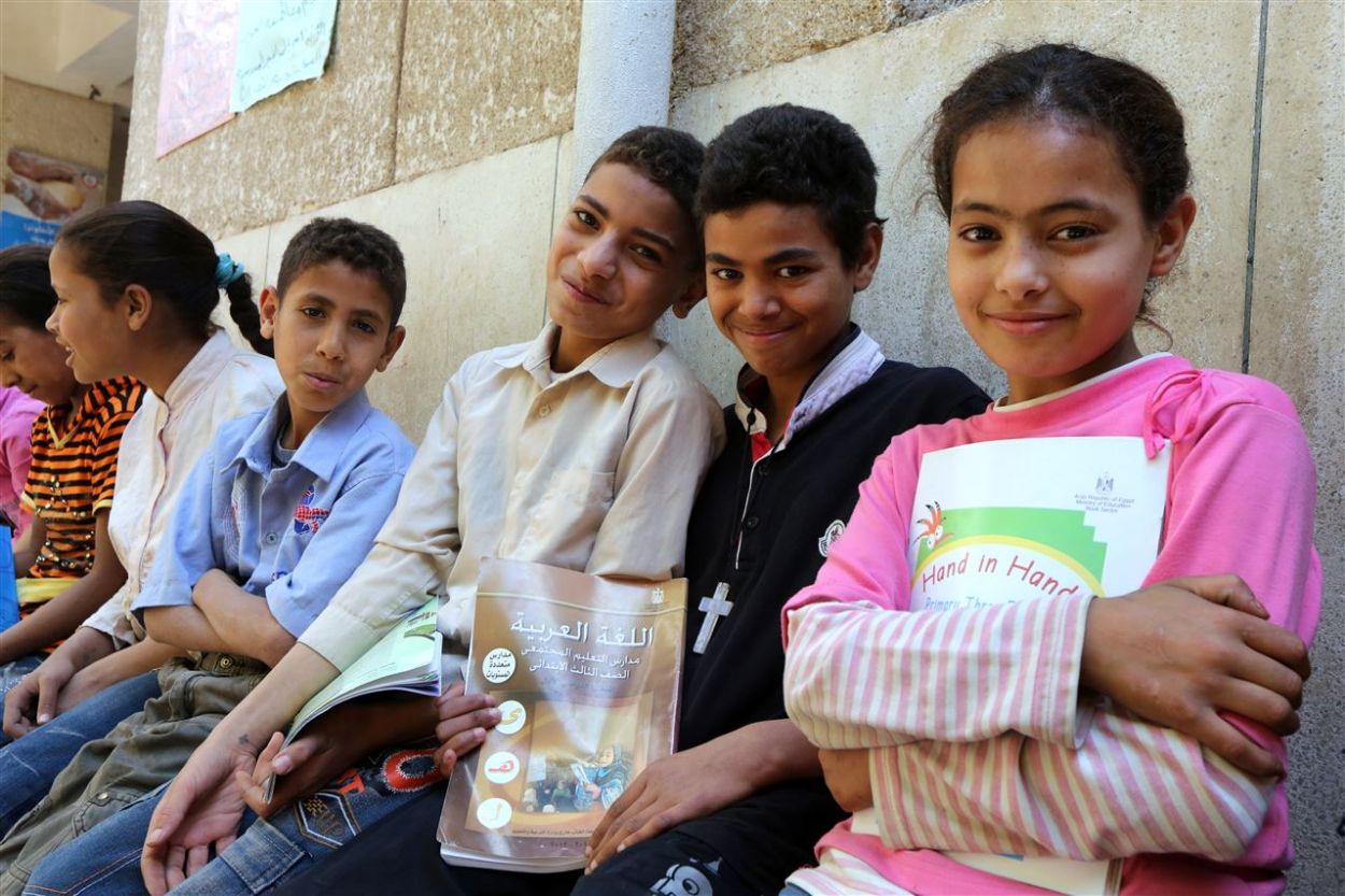 Sechs arabische Kinder sitzen nebeneinander auf einer Bank. Ein Junge trägt ein Kreuz um den Hals, ein Mädchen hält eine deutschsprachige Broschüre in der Hand.