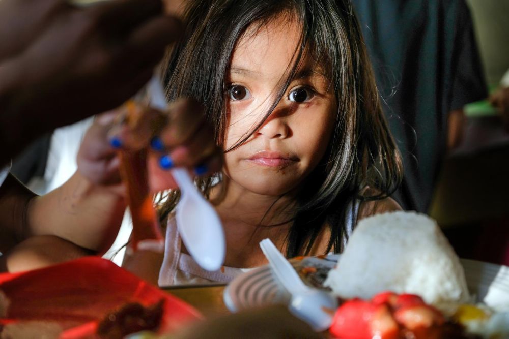 Ein Mädchen aus den Philippinen sitzt vor einem Teller mit Reis und isst.
