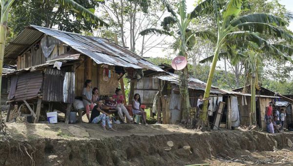 Menschen sitzen auf der philippinischen Insel Mindanao vor ihren ärmlichen mit Wellblech bedeckten Behausungen. Dazwischen wachsen Palmen.