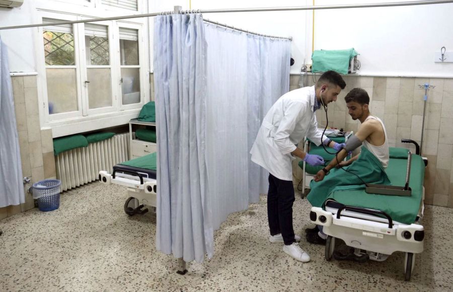 Ein junger Mann sitzt auf einem Krankenbett. Er wird von einem vor ihm stehenden Arzt versorgt