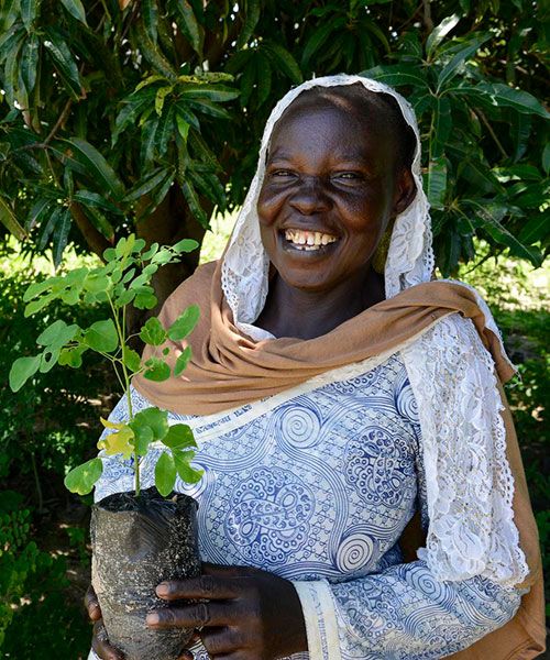 Frau hält einen Setzling in der Hand und lacht den Betrachter an