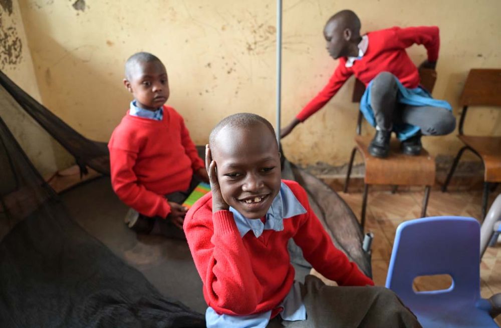 Drei Schulkinder mit roten Schulpullovern spielen in einem Klassenzimmer.