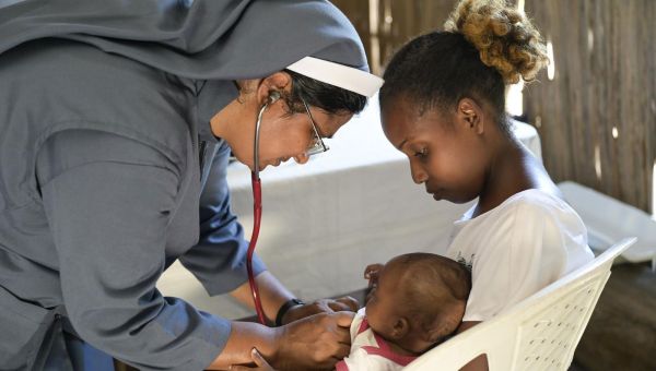 Schwester Jain Mary untersucht ein Baby auf dem Schoß der Mutter