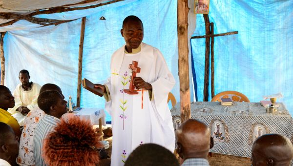 Ein afrikanischer Priester steht vor der Gemeinde in einem provisorischen Kirchenraum.