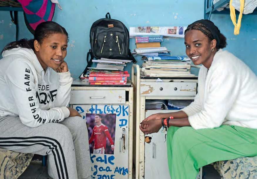 Zwei junge Frauen sitzen sich im Mädchenschlafsaal des Waisenhauses St. Clare in Harar in Äthiopien auf ihren jeweiligen Betten gegenüber. Auf ihren nebeneinanderstehenden Nachttischen im Hintergrund stapeln sich Bücher und Hefte.
