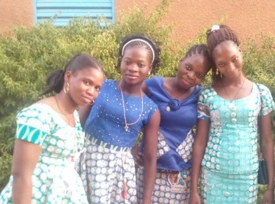 Vier Mädchen aus Burkina Faso stehen freundschaftlich nebeneinander, die Köpfe geneigt und lächeln in die Kamera.