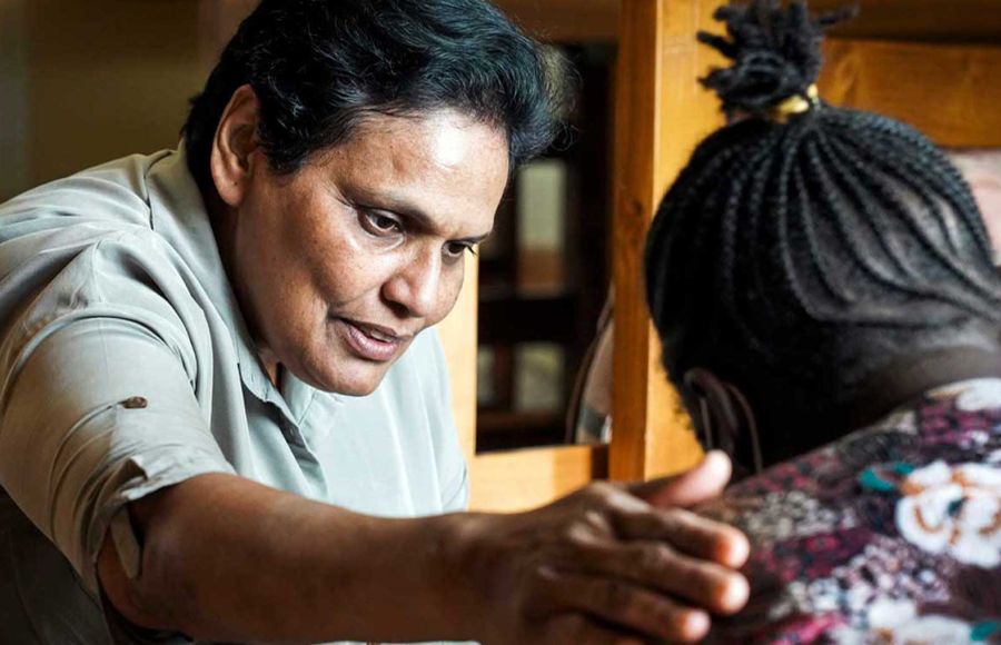 Eine Ordensschwester legt tröstend den Arm auf die Schulter einer jungen Frau, die im Bild nur von hinten zu sehen ist.