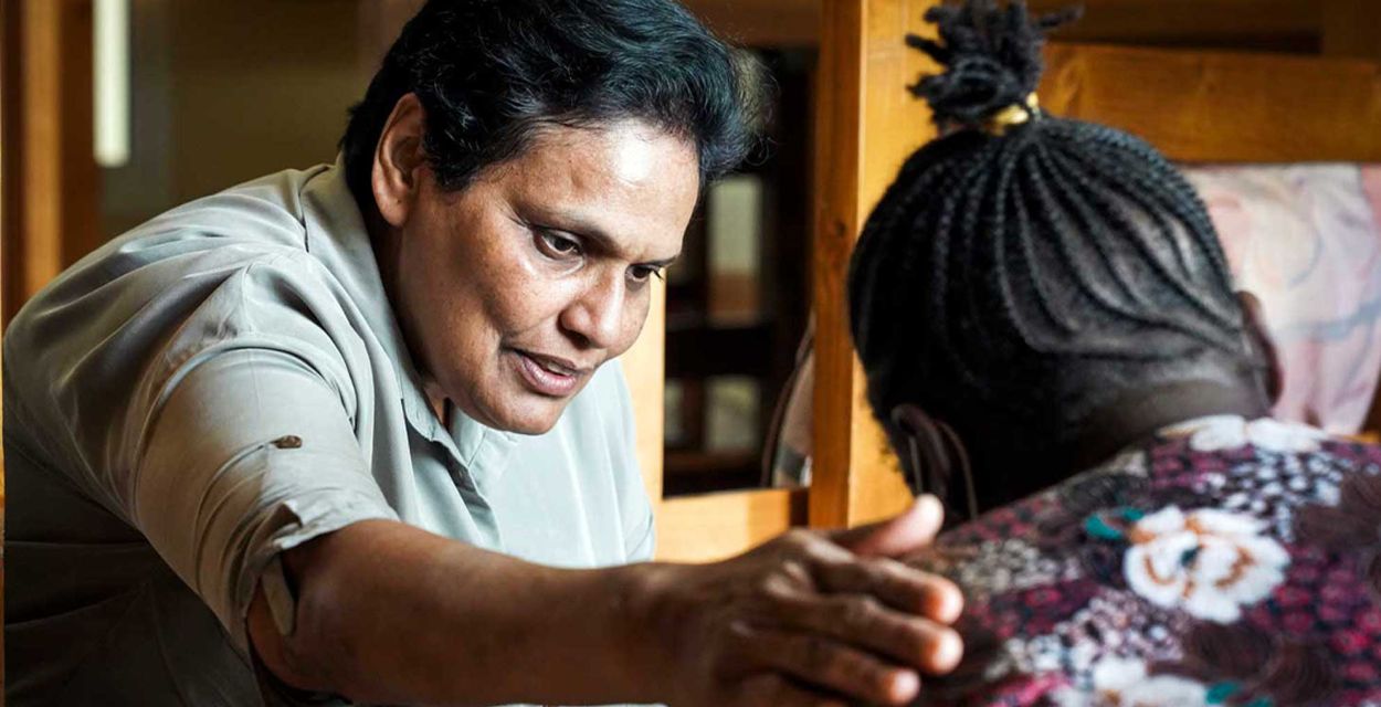 Die Mitarbeiterin eines Schutzhauses legt einer anderen Frau, die nur von hinten zu sehen ist, eine Hand auf die Schulter, um sie zu trösten.