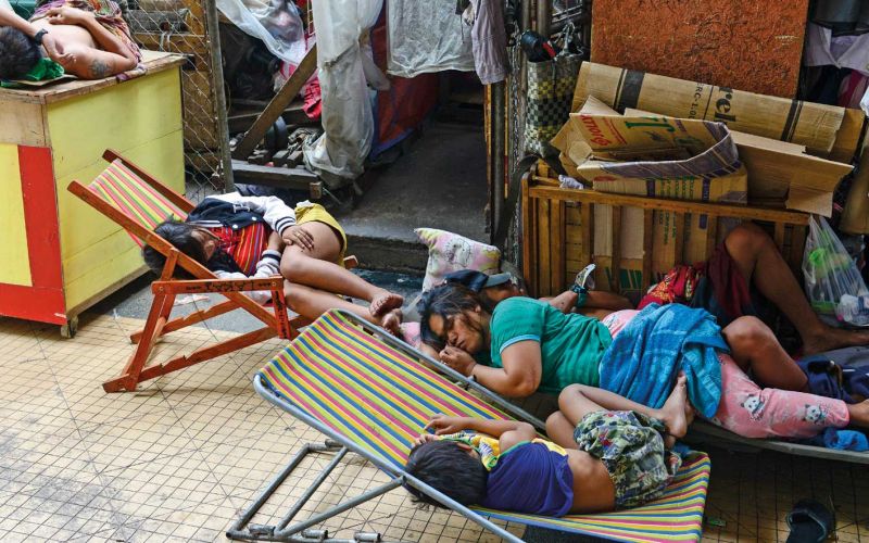 Eine Frau schläft mit ihren Kindern am Rand einer Straße in Manila auf einem Bretterverschlag. Zwei Kinder schlafen auf Klappstühlen.