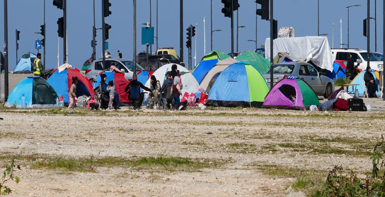 Bunte Zelte stehen auf einem sandigen, kärglich bewachsenen Platz. Im Hintergrund zahlreiche Ampeln und der strahlend blaue Himmel.